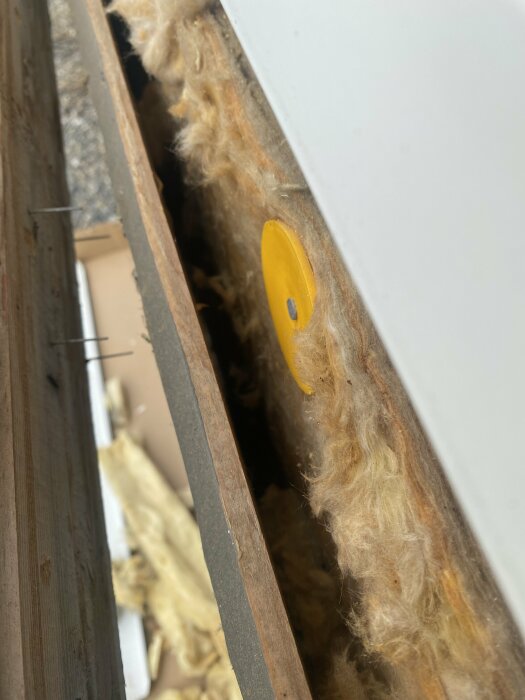 Isoleringsmaterial med en gul plastbricka fastsatt inuti en väggkonstruktion under ett byggprojekt.