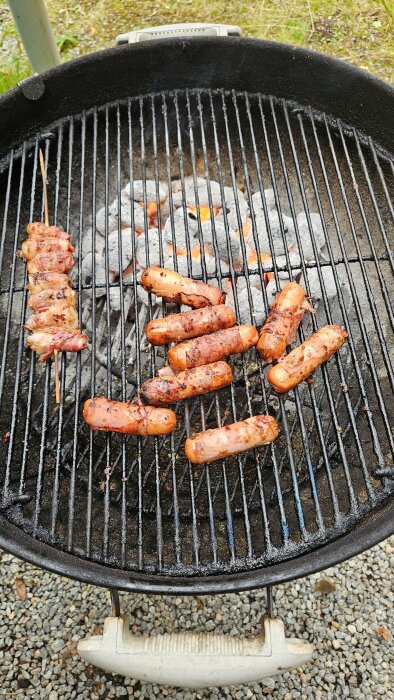 Grill med Lidls korvar med inbyggd ost och bacon, samt extra bacon, över glödande kol. Korvarna ser grillade och krispiga ut.