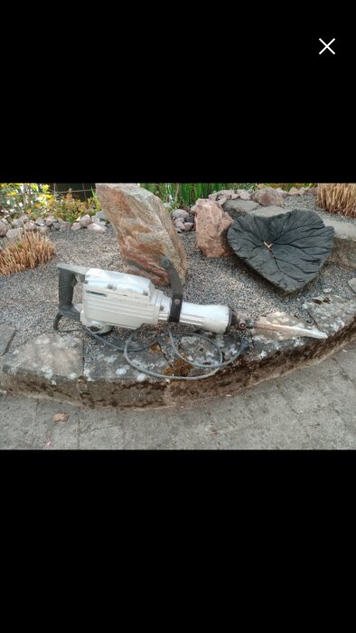 Bilmaskin ligger på en stenbädd med stenar i bakgrunden i en trädgård.