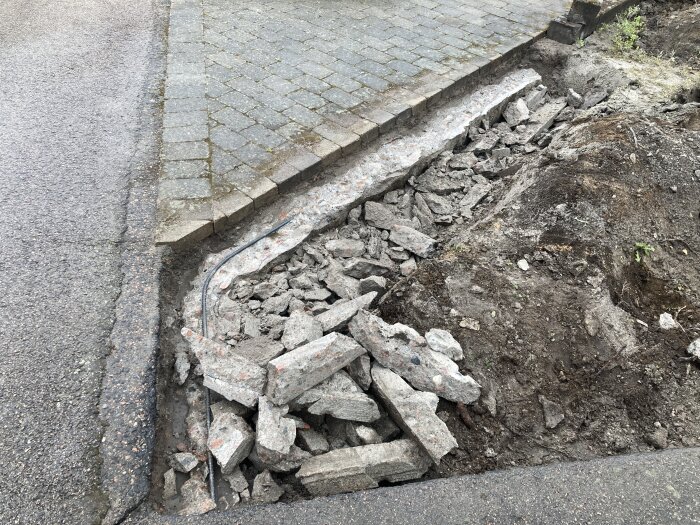 En trasig betongsockel ligger på marken bredvid en stenbelagd trottoar efter att ha blivit nedmonterad med vinkelslip och bilmaskin.