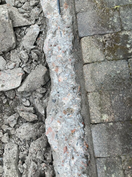 Bärande grundsockel på byggarbetsplats, nedhuggen under nivån för stenmjöl, omgiven av betongrester och stenar, intill en stenlagd gång.