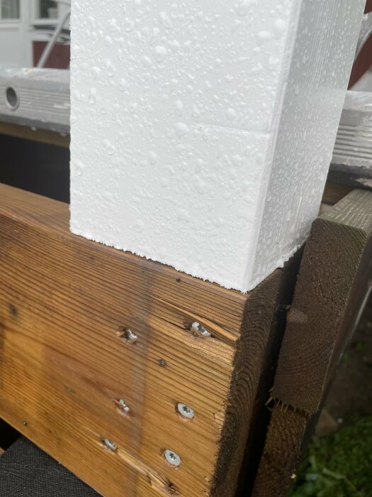 Vitmålad limträstolpe i 115x115 mm vilar på plint med takpapp emellan, stöttad av bärlina. Stolpen är våt av regn, inlägg handlar om oro för röta.