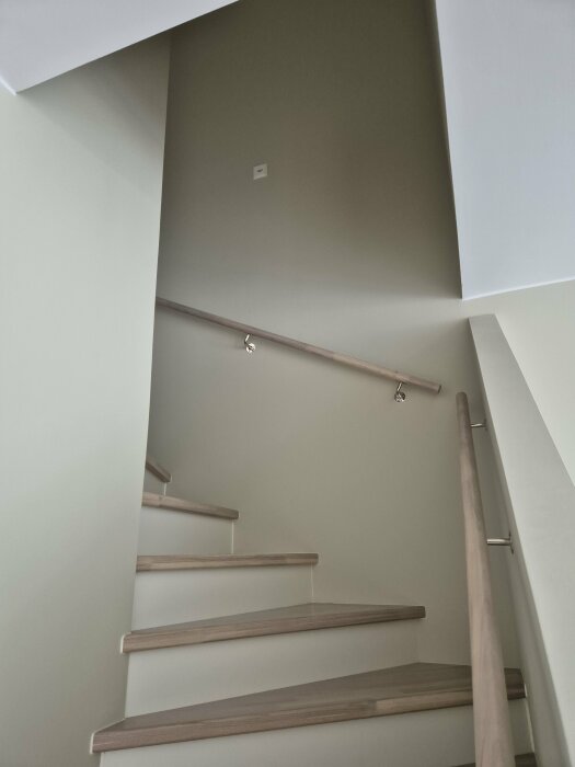 Spiraltrappa med smala steg och ett räcke som följer trappstegen uppåt. Ljusa väggar och trappsteg med träkanter.