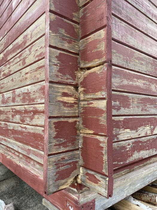 Närbild av en bods hörn med röd färg som flagnar och synlig rötskada i trähörnet.