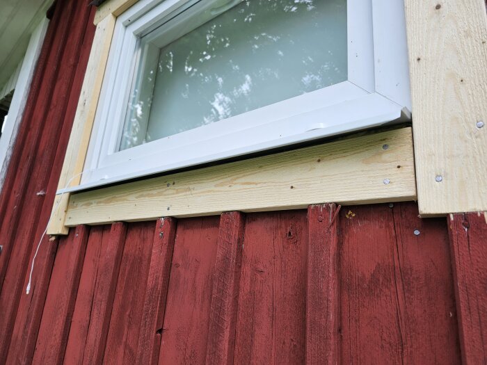 Bytt fönster med synlig glipa på cirka 1 cm under fönsterblecket mot den rödmålade träpanelen.