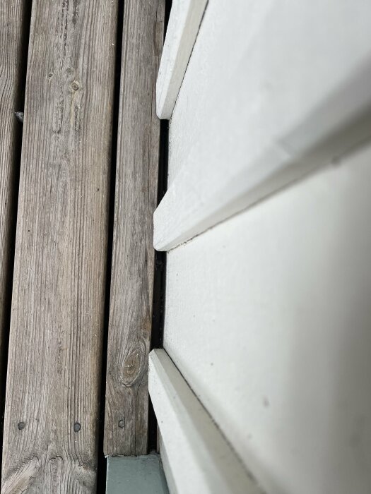Närbild på träaltan som är fäst direkt mot en vit träfasad, vilket orsakar vattenproblem intill fasaden.