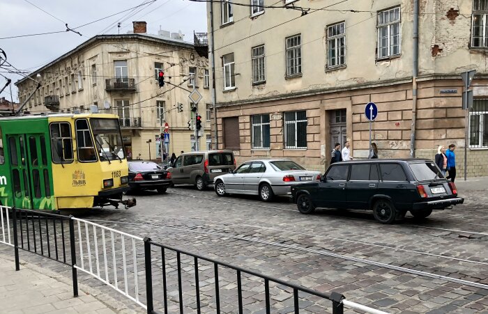 Spårvagn och bilar, inklusive en svart Lada, på en stadsgata i Lviv, Ukraina. Gamla byggnader och gående syns i bakgrunden.