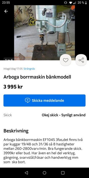 Arboga bänkmodell borrmaskin i en verkstad med andra verktyg och maskiner i bakgrunden. Prislapp och beskrivning är synliga på skärmen.