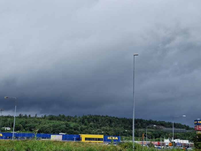 Mörk himmel över IKEA-varuhus i Uddevalla med parkeringsplats och skog i bakgrunden.