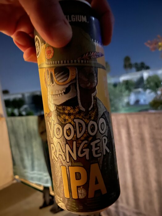 En person håller i en burk Voodoo Ranger IPA öl på en balkong på kvällen.