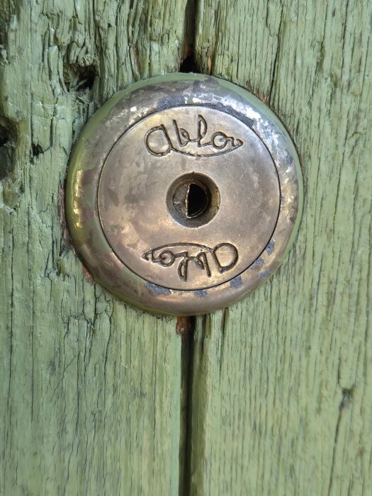 Gammalt dörrlås från märket Abloy monterat i sliten grön träpanel.