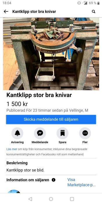 Gammal grön kantklippmaskin med trä- och metallkomponenter står på grovt trägolv, med rostande detaljer och remmar på maskinen.