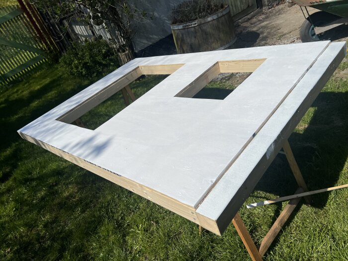 Ett bord utomhus med en träskiva på, med två utskurna rektangulära hål och målade med vit färg, för ett byggprojekt av värpreden.