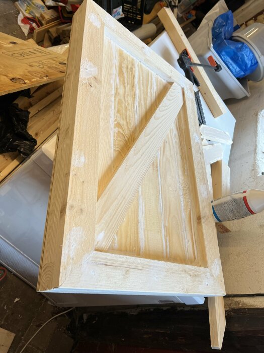 En nybyggd dörr av trä på ett arbetsbord, gjord av 45x45-reglar och täckt med plywood och råspont. Trälim, såg och andra verktyg ligger runtomkring.