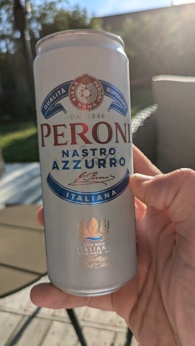 En hand som håller en burk Peroni Nastro Azzurro öl utomhus i dagsljus.