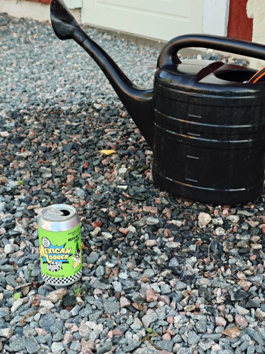 Bevattningskanna och en burk med ölen "Mexican Lager" på en grusyta.