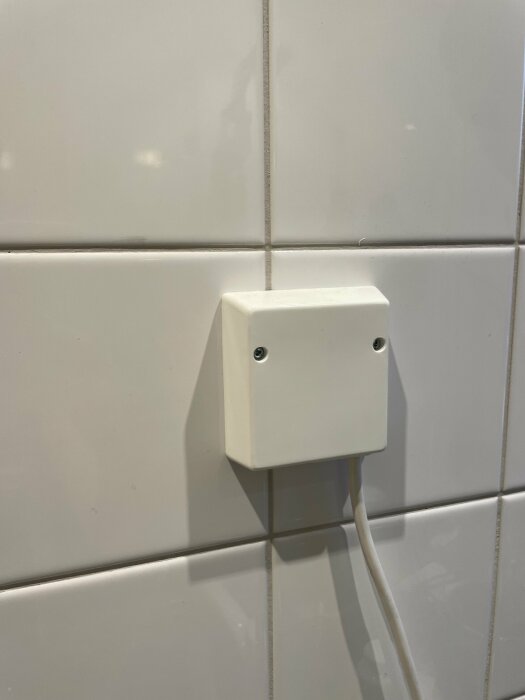 Vit eluttag/dosa på en vit kaklad vägg i ett badrum med en sladd nedåt.