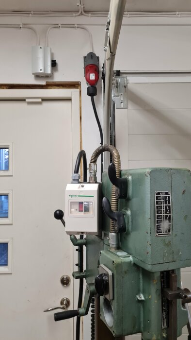 En pelarborrmaskin med nyinstallerat elektriskt styrsystem, inklusive tryckströmställare och ledningar, monterade bredvid en dörr i ett garage.