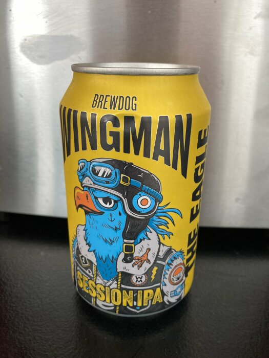 En gul ölburk av märket Brewdog Wingman Session IPA med en tecknad blå örn i pilotkläder på framsidan.