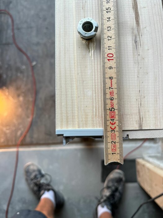 Tröskel till ytterdörr från Kaski med en kant på aluminiumdelen som sticker ner 5 mm, mätt med en tumstock på en arbetsbänk. Fötterna av personen som monterar syns i bildens nederkant.