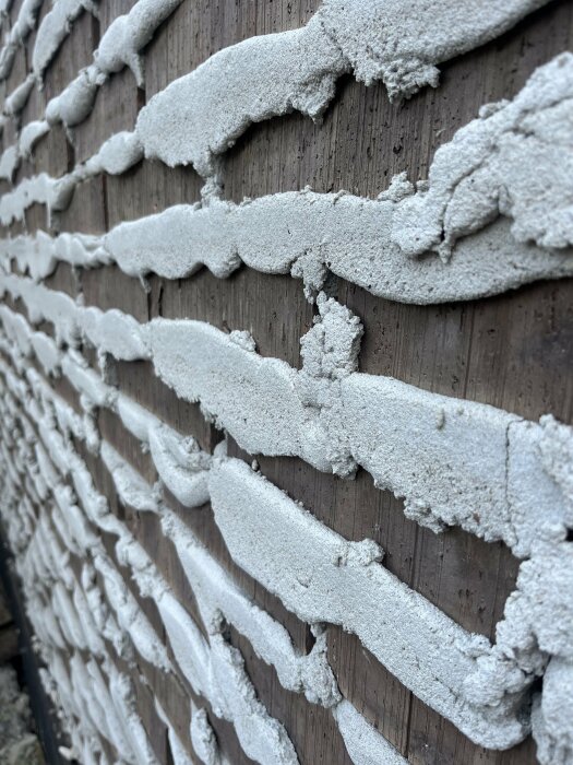 Närbild av en vägg med oregelbundna lager av murbruk på en träyta.