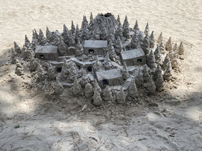 Sandstaty föreställande en by med hus och träd omgiven av en skog, byggd på en sandstrand.