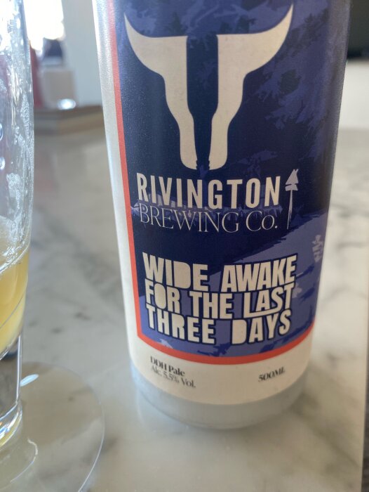 En ölburk från Rivington Brewing Co. med etiketten "Wide Awake For The Last Three Days" DDH Pale Ale, 5,5% vol, 500 ml, och ett halvtomt glas öl bredvid.