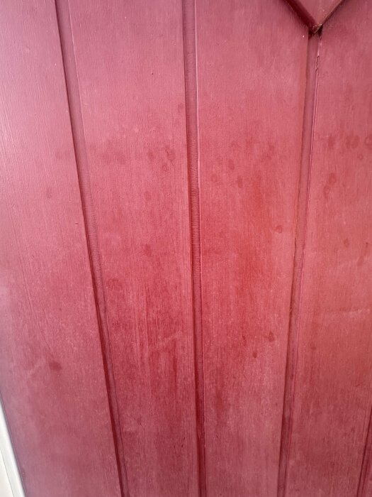 Närbild på en röd dörr, målad med linoljefärg. Färgen ser solblekt och mjölkig ut på ytan, med fläckiga partier.