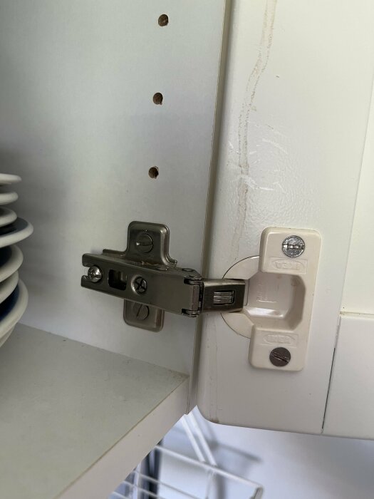 Gångjärn monterat på en vit IKEA skåpsdörr från 90-talet, frågar om möjligheten att installera soft close eller byta beslag.