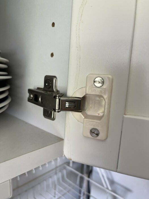 Närbild på ett köksskåp från IKEA med skåpsgångjärn från 90-talet, där användaren undrar om man kan installera soft close eller byta beslagen.