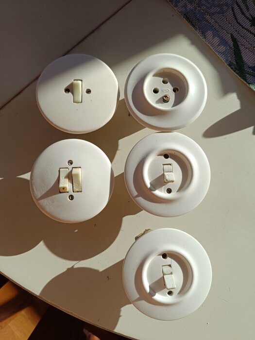 Fem äldre vita strömbrytare och eluttag ligger på ett bord belyst av solljus, erbjuds gratis mot betald frakt på 80 kr.
