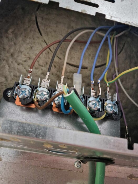 Anslutningar och kablar på baksidan av en ugn som behöver bytas ut, flera färgade ledningar är kopplade till terminalblock.