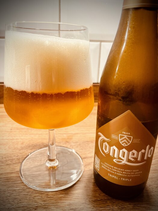 En flaska Tongerlo Tripel belgisk öl bredvid ett glas fyllt med skummande gyllene öl.