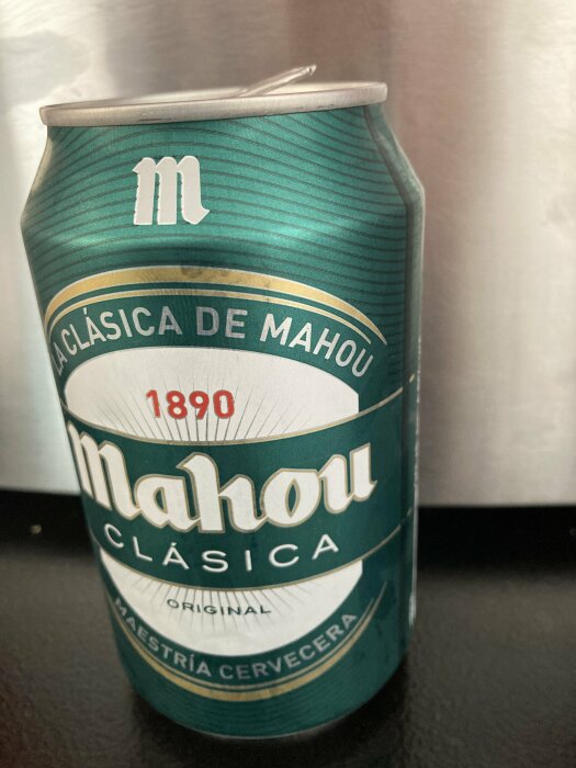 En burk Mahou Clásica öl med text "La Clásica de Mahou 1890" mot en metallisk bakgrund.