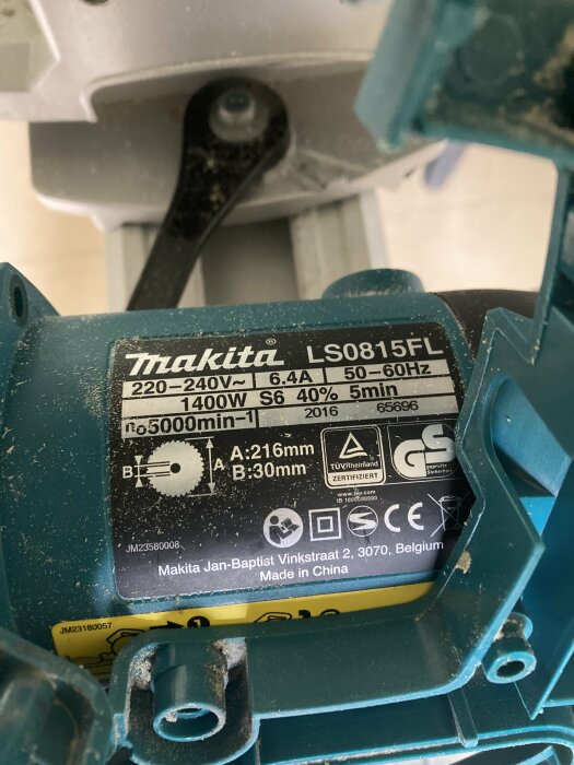 Närbild av en blå elektrisk sågs komponenter och etikett med specifikationer, inklusive modellnummer Makita LS0815FL, kraft 220–240V, 1400W.