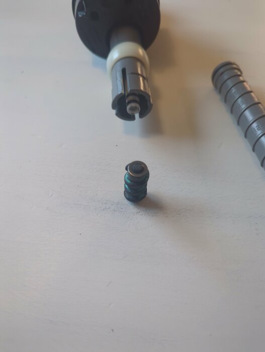 Närbild på en demonterad flottör i en Gustavsberg-toalett. Delarna visar en "gummiskruv", vita och gråa rör på ett vitt underlag.