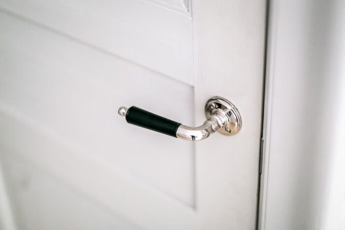 Kromad dörrhandtag med svart grepp, monterad på en vit dörr.