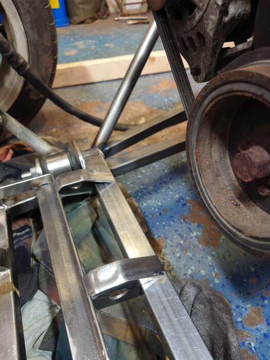 Närbild på en del av en metallram och ett hjul i ett garage, en del av ett bygg- eller renoveringsprojekt.
