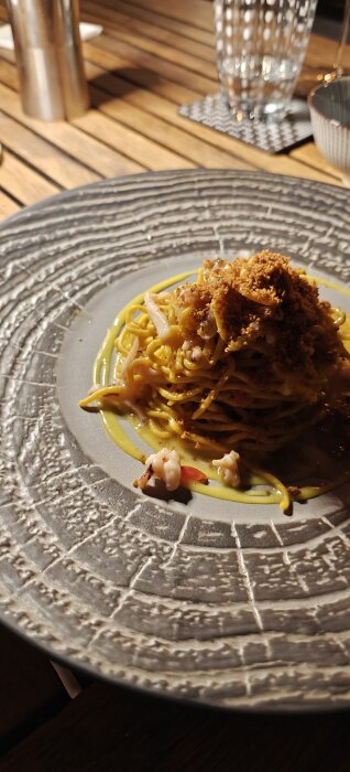 En tallrik med pasta, sannolikt seafood pasta, delvis dekorerad med sås och ströbröd, serverad på ett matbord.