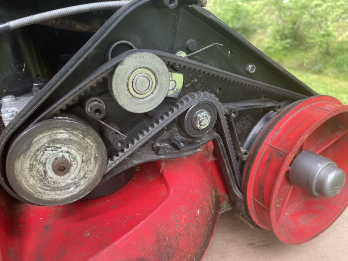 Närbild av en röd maskin med synliga remskivor och hjul, där ett hjul längst till vänster har justeringsmöjligheter.