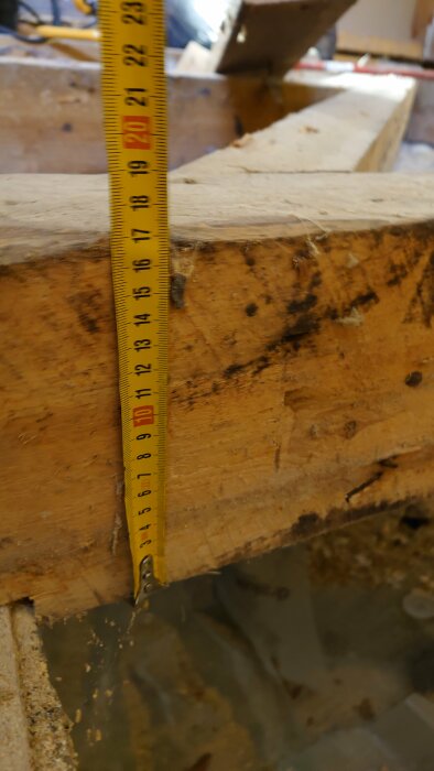 Träbjälke med en måttstock som visar 20 cm i horisontell mätning; bilden är tagen i samband med renovering av ett badrum.