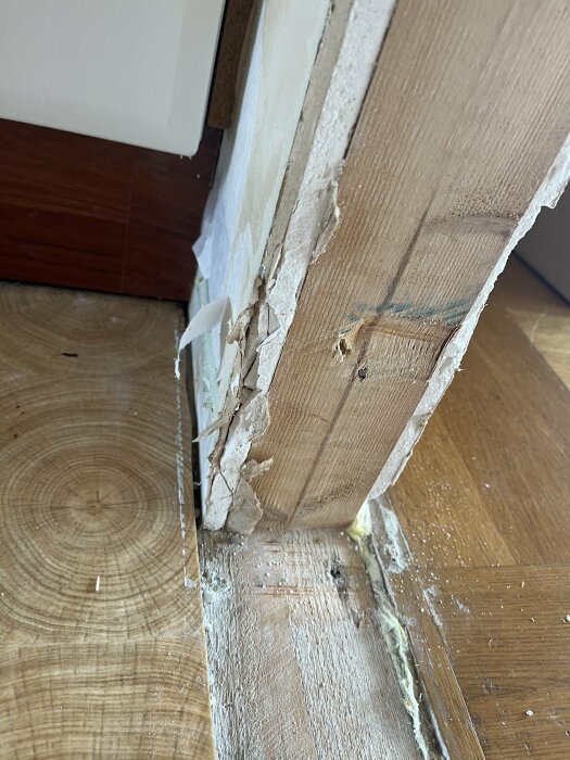 Trasiga gipsskivor och en ohyvlad träram runt en ny öppning i en vägg, med exponerat trä på golvet och en kant av gips som behöver repareras.