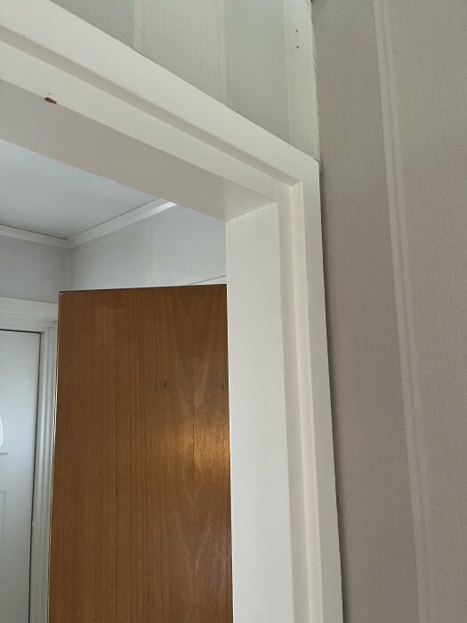 Nyupptagen öppning i en vägg med synligt vitt dörrkarm, omgivande gipsskivor verkar skadade på flera ställen i kanten. Bakom ses en brun dörr.