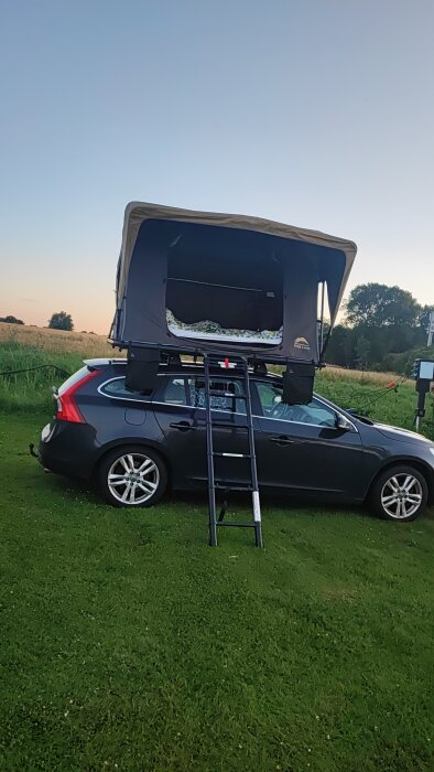 Bil med ett Wild Land Normandy 140 taktält uppställd på en campingplats i solnedgång. Tältet är monterat på en V60 med stege för att komma in.