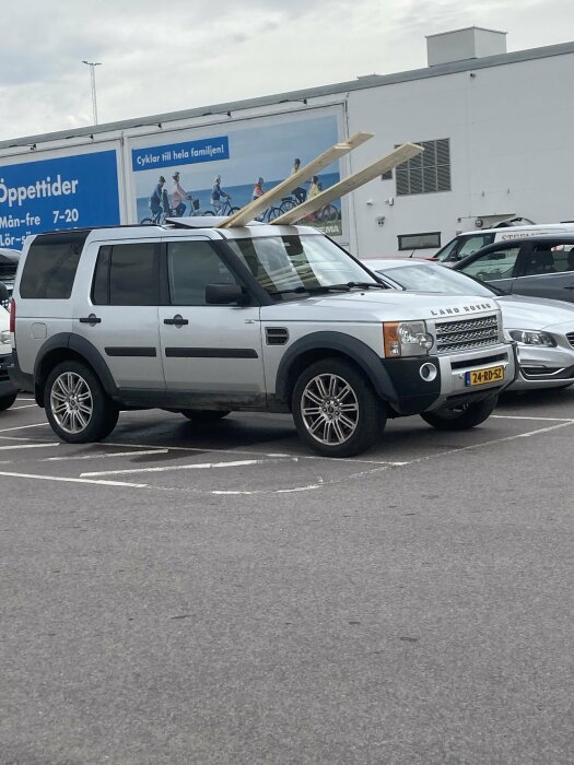 Land Rover Discovery på parkeringsplats med långa plankor utstickande genom passagerarfönstret.