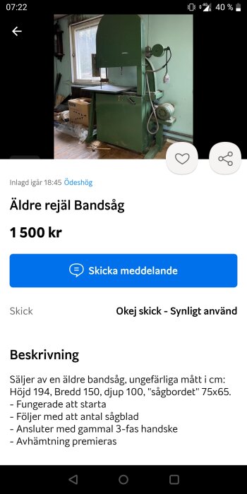 Äldre grön bandsåg till salu, stående i ett rum med ett fönster. Andra föremål, som kartonger och träspill, är synliga i bakgrunden.