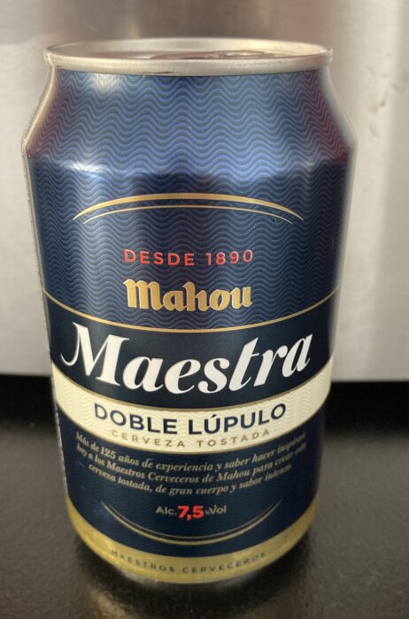 En burk Mahou Maestra Doble Lúpulo öl, 7,5% vol, med mörkblå etikett, text på spanska och gulddetaljer.