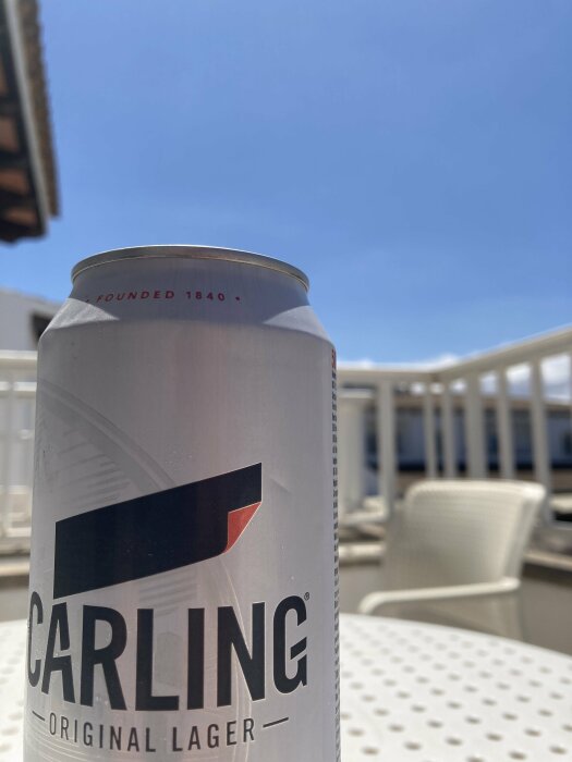 En burk Carling Original Lager på ett utebord i solskenet med blå himmel i bakgrunden.