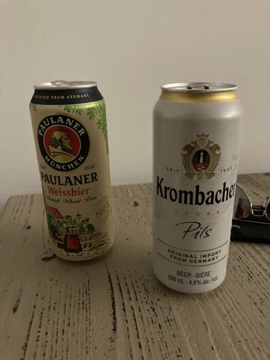 Två burkar öl på ett bord, en Paulaner Weissbier till vänster och en Krombacher Pils till höger.