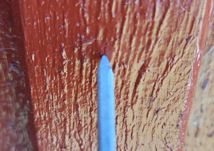Närbild på en spik som är inslagen i ett rödbrunt trästycke.